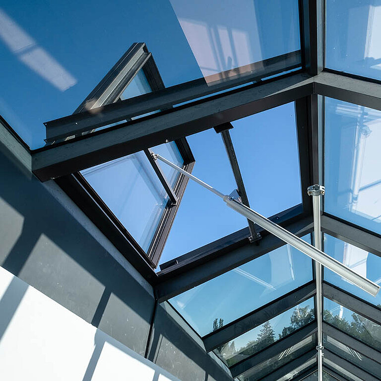 Innenansicht eines geöffneten LAMILUX Glasdach RWA mit geneigter Verglasung, sichtbarer Tragkonstruktion und Blick in den Himmel