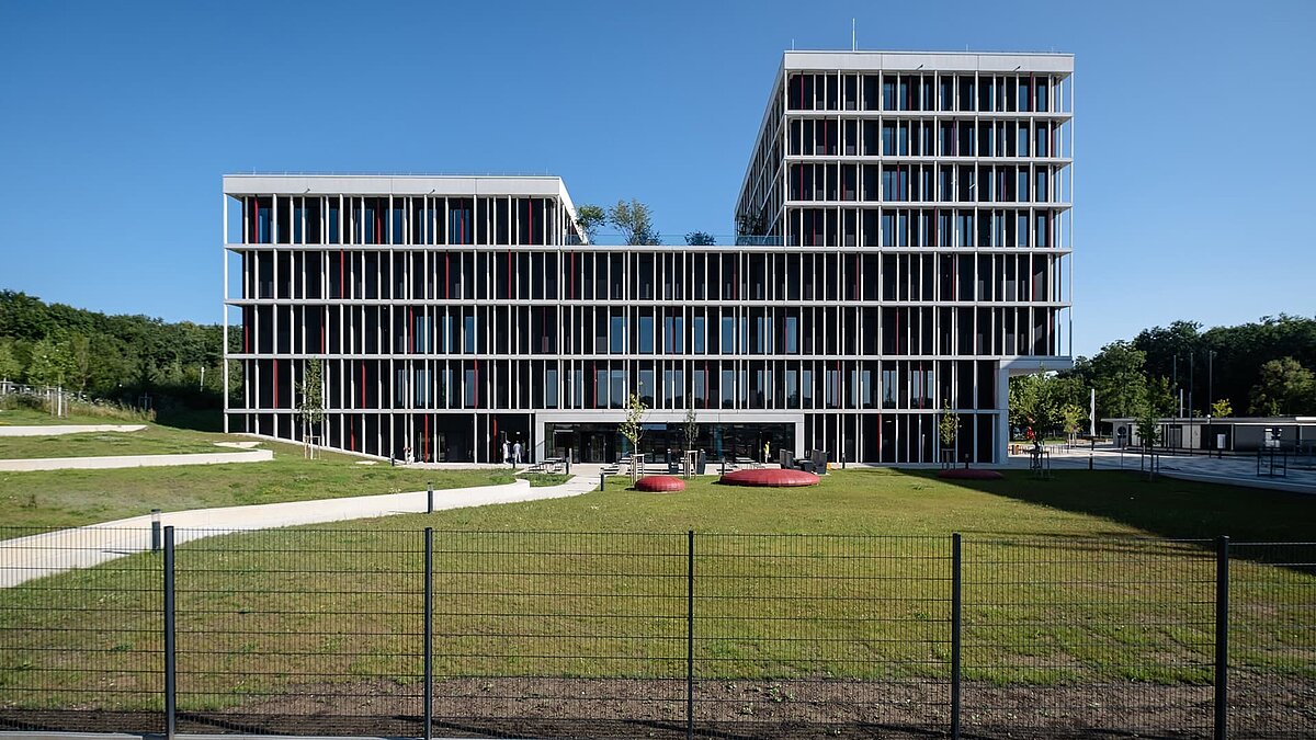 Modernes Bürogebäude mit Glasfassade und grünem Außenbereich bei Sonnenschein