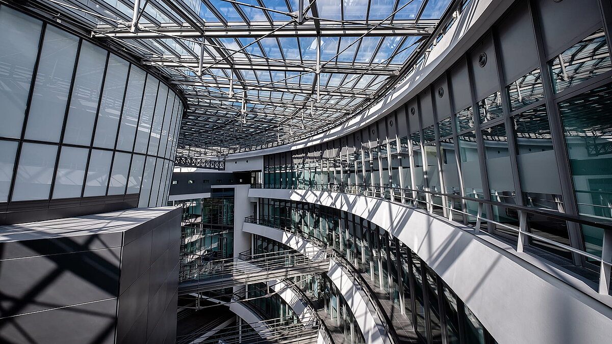 Innenansicht des BMW Group Forschungs- und Innovationszentrums (FIZ) mit geschwungenen Glasfassaden und einem weitläufigen Glasdach, das Tageslicht in die modernen Bürobereiche leitet.