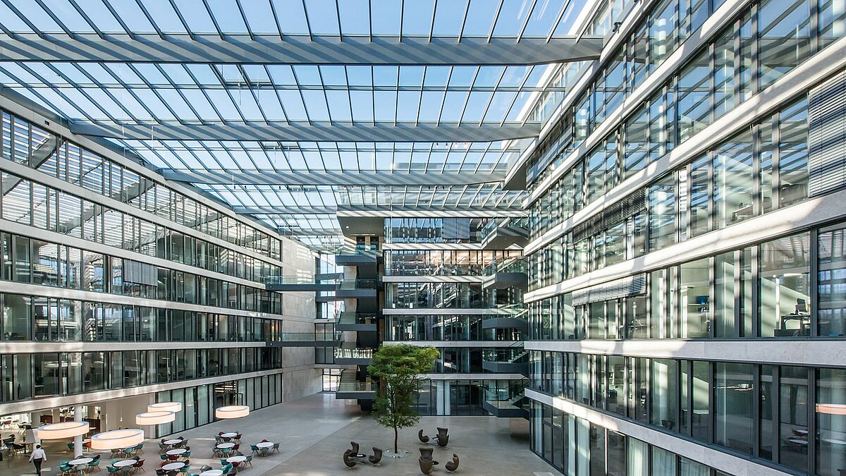 Modernes Atrium des FGS Campus mit großflächigem Glasdach, lichtdurchfluteten Räumen, mehreren Stockwerken und Sitzmöglichkeiten im offenen Bereich.