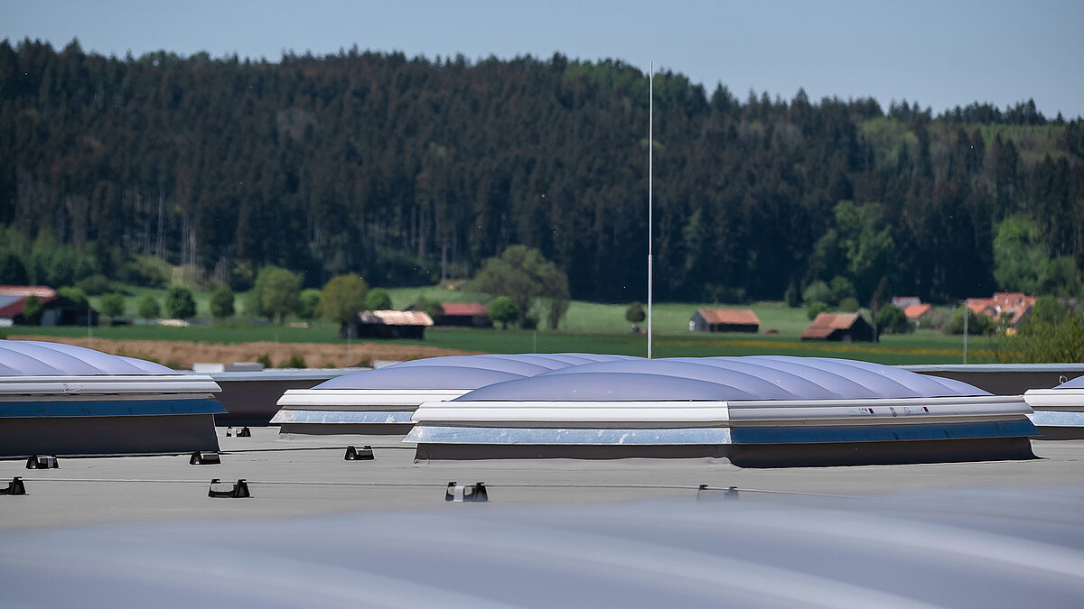 LAMILUX Lichtkuppeln F100 W auf dem Dach der Produktionshalle des Bauunternehmens Unglehrt, umgeben von ländlicher Landschaft mit Bäumen und Bauernhäusern.
