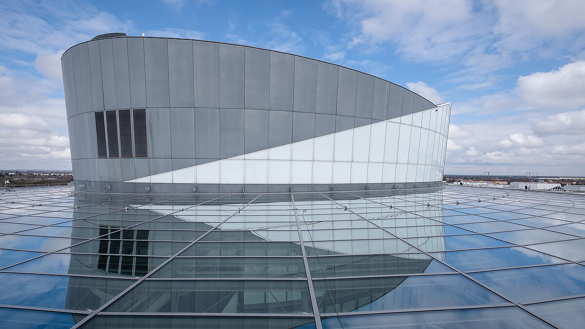 Außenansicht des BMW Group Forschungs- und Innovationszentrums (FIZ) mit markanter Architektur, bestehend aus einer geschwungenen Fassade und einem weitläufigen Glasdach.