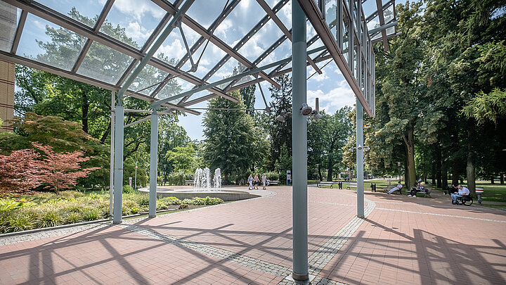 Überdachte Außenfläche mit filigraner Stahl-Glas-Konstruktion im Park.