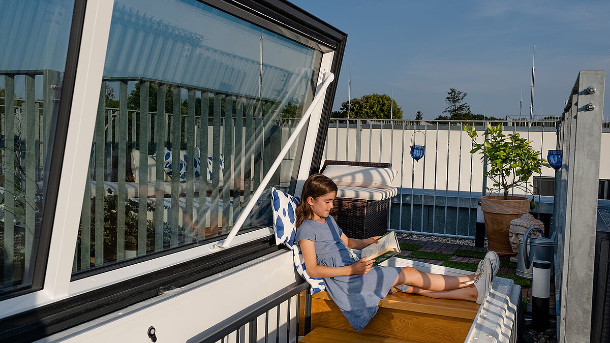 Mädchen liest ein Buch auf der Dachterrasse eines Townhouses in Berlin, neben einem geöffneten Flachdach Ausstieg.