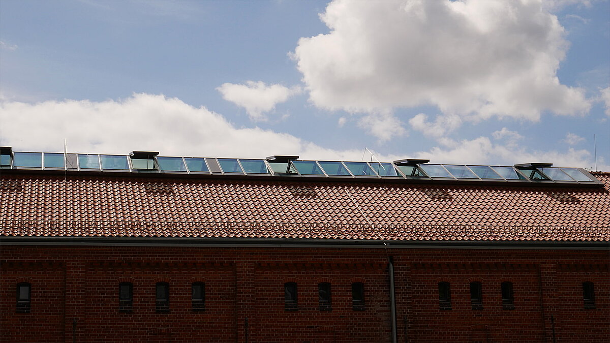 Rotes Ziegeldach mit modernen Glasdachfenstern der Leibniz-Universität Hannover unter blauem Himmel mit Wolken.
