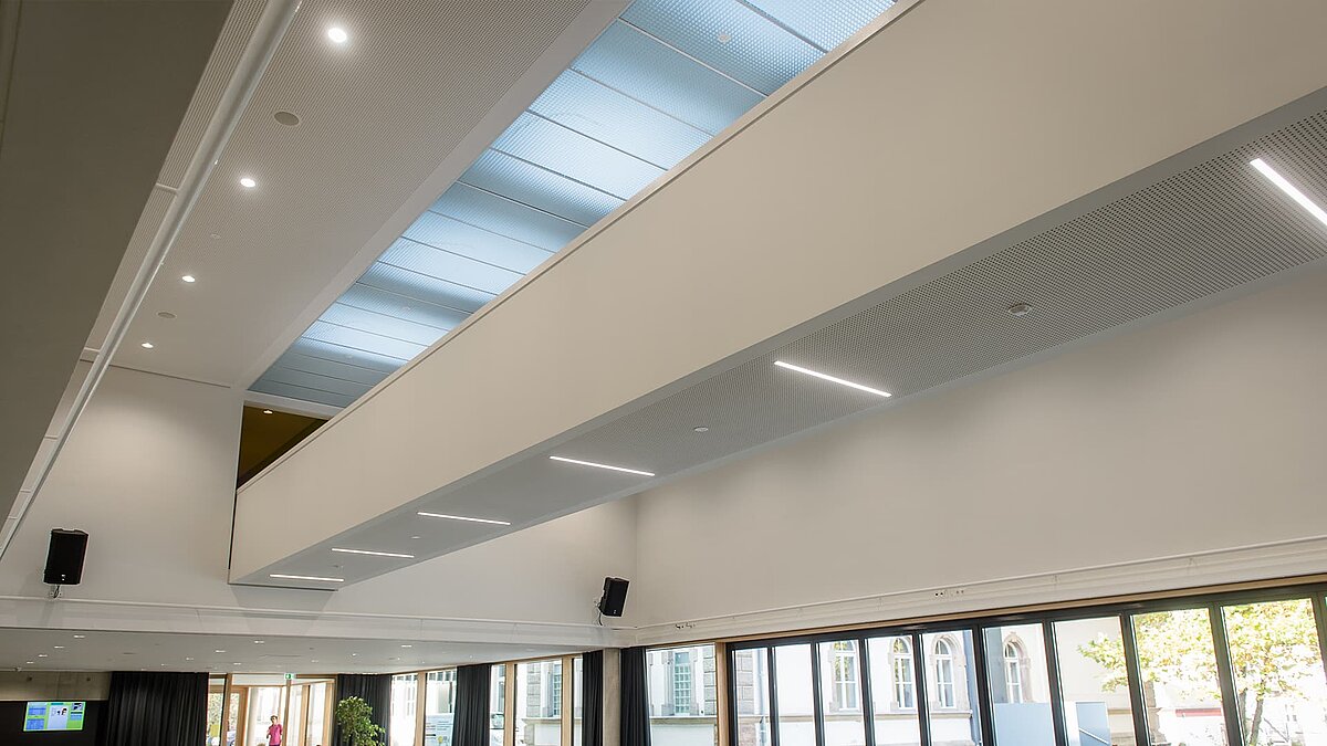 Innenansicht der Aula des Markgraf-Georg-Friedrich-Gymnasiums in Kulmbach mit Flachdach-Fenstern und moderner Beleuchtung.