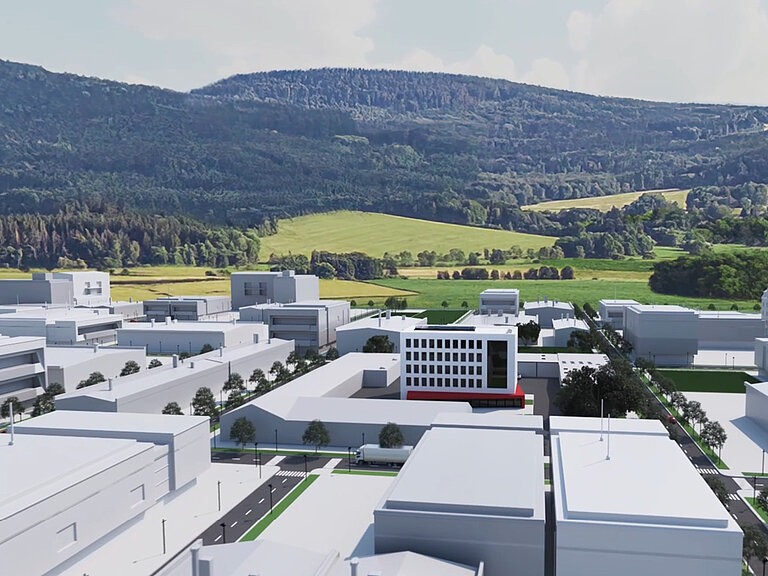 Luftaufnahme eines Industrie- und Gewerbekomplexes mit mehreren Hallen und Bürogebäuden, umgeben von grüner Landschaft und Hügeln