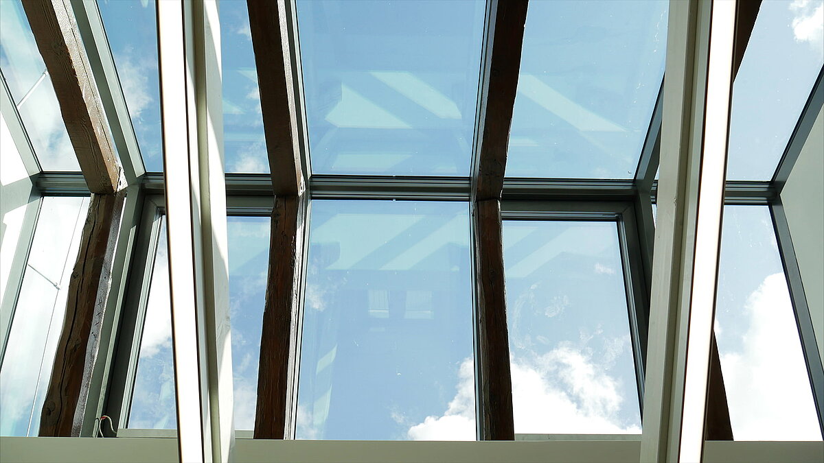 Modernes Glasdach der Leibniz-Universität Hannover mit sichtbaren Holzbalken und Himmelreflexionen.