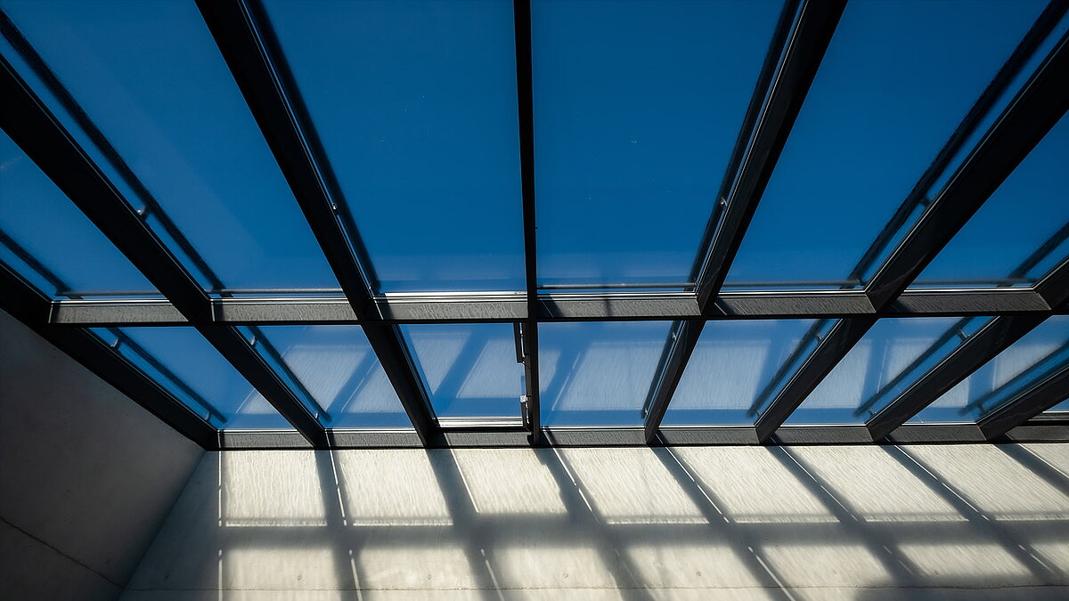 Detailansicht des Glasdachs der Bertha-von-Suttner-Realschule in Köln mit klarer Sicht in den blauen Himmel.