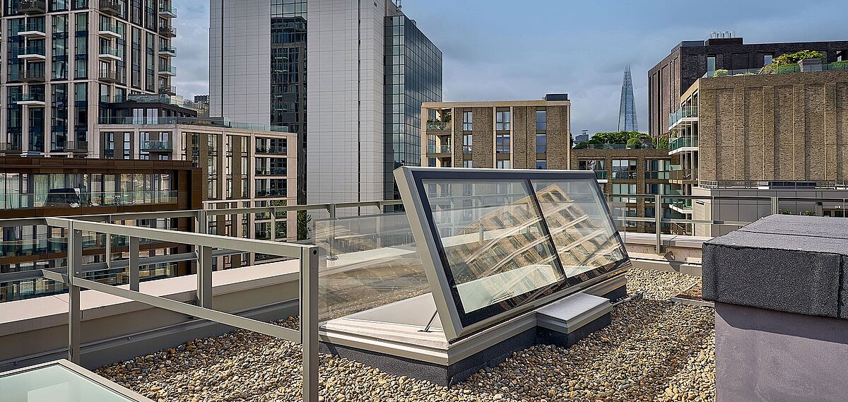 LAMILUX Flachdach Ausstieg auf dem Dach der Mulberry Academy London, umgeben von Kiesbelag und moderner Architektur, im Hintergrund das Hochhaus The Shard.