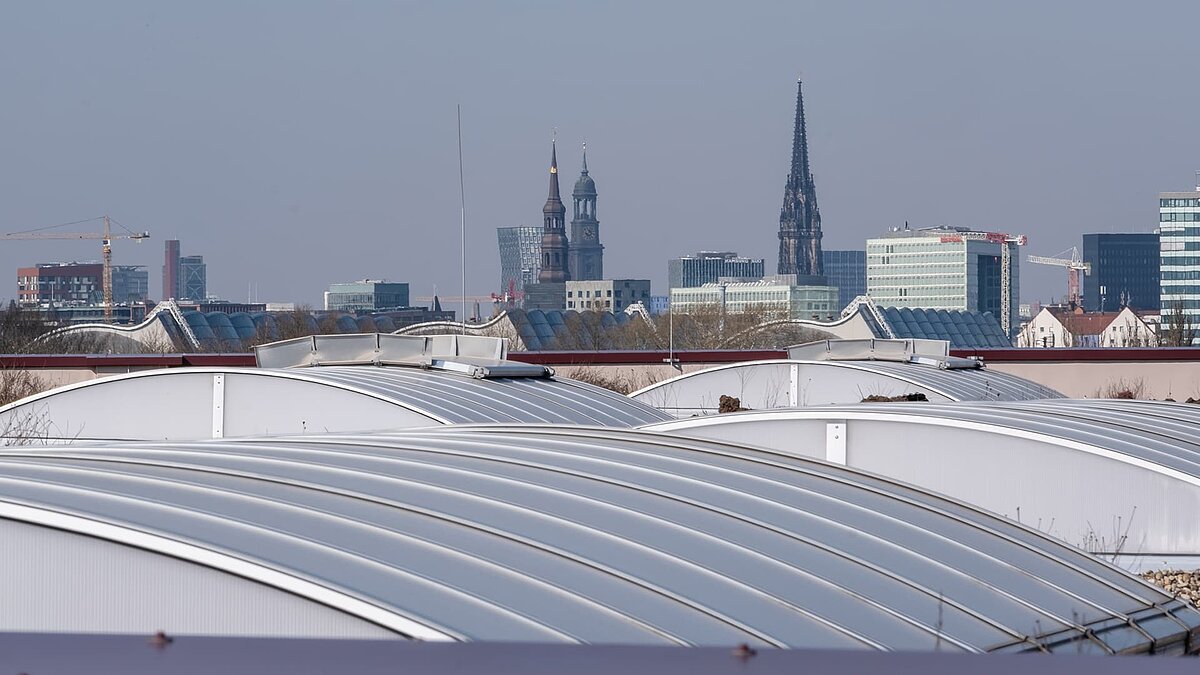 Flachdach mit gebogenen Lichtbändern des Opernfundus der Hamburgischen Staatsoper, im Hintergrund die Skyline von Hamburg.