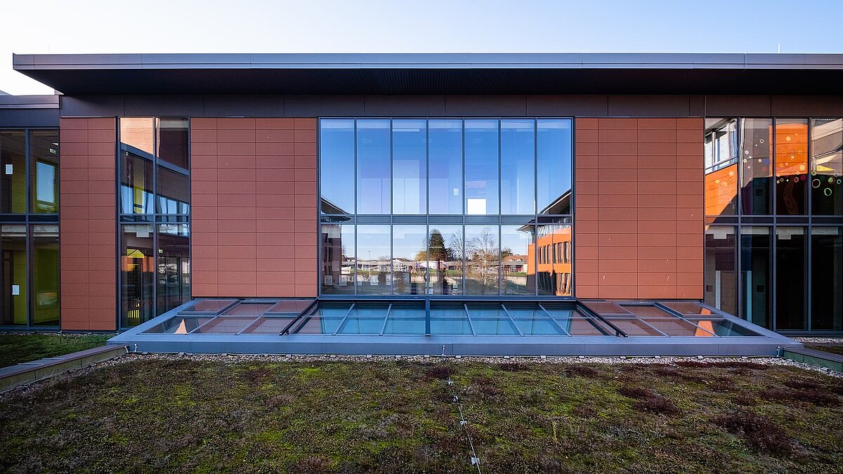 Außenansicht des Schulzentrums Rehau mit einem LAMILUX Glasdach PR60 über einer begrünten Dachfläche.