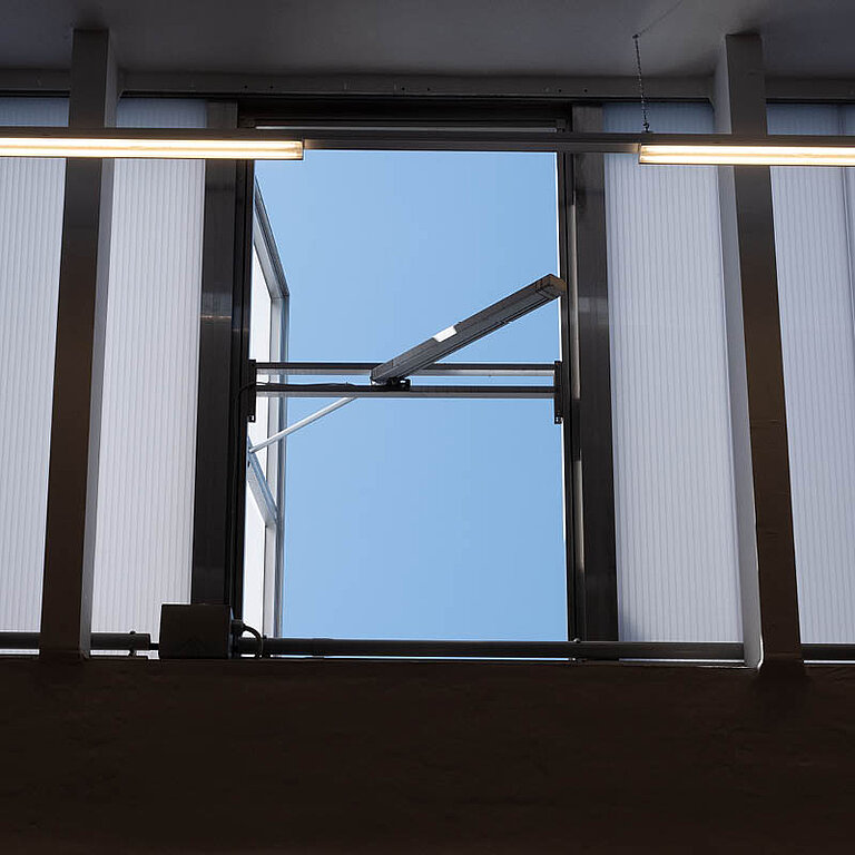 Innenansicht eines geöffneten LAMILUX Lichtband W|R RWA mit seitlich aufgestelltem Flügel und Blick nach außen