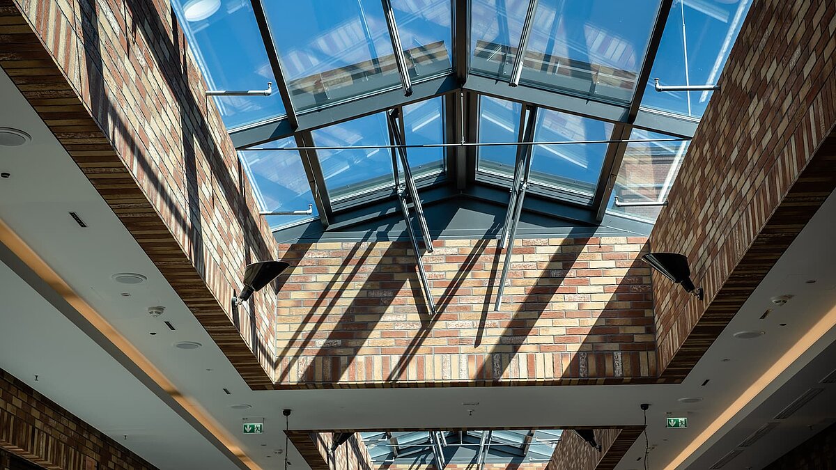 Glasdach des Schultheiss Quartiers in Berlin-Moabit, mit natürlichem Lichteinfall und Ziegelwänden, die Schattenmuster erzeugen.