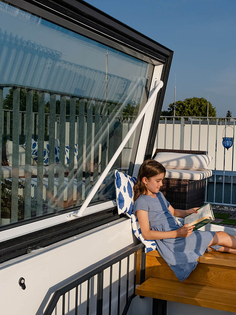 Geöffneter LAMILUX Flachdach Ausstieg Komfort Swing mit seitlich schwenkender Verglasung als direkter Zugang zu einer genutzten Dachterrasse mit Aufenthaltsbereic