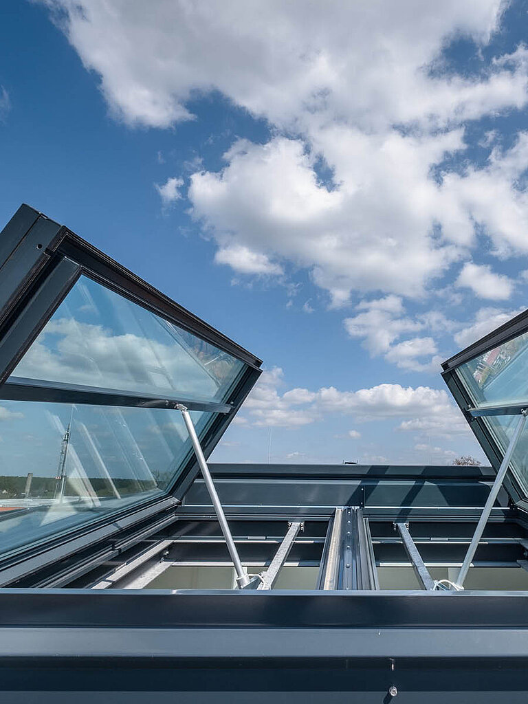 Geöffnete Flachdachfenster mit geneigter Verglasung auf Flachdach, Ansicht von unten vor blauem Himmel mit Wolken