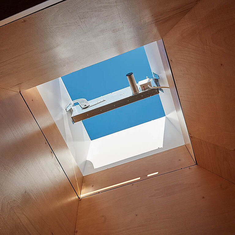 Innenansicht eines LAMILUX Flachdach Fenster FE RWA mit geöffneter Verglasung, sichtbarer Antriebstechnik und Blick in den Himmel