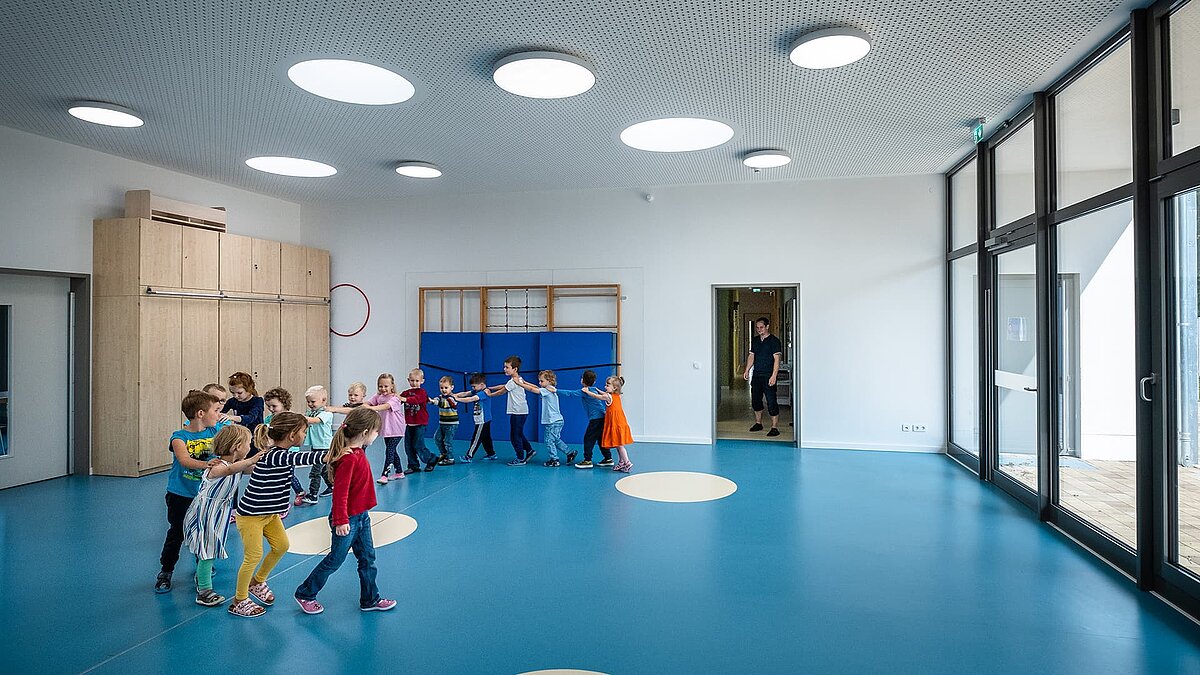 Turnhalle der Kindertagesstätte Sonnenfeld in Wandlitz mit spielenden Kindern, blauer Boden, runde Oberlichter und moderne Ausstattung.