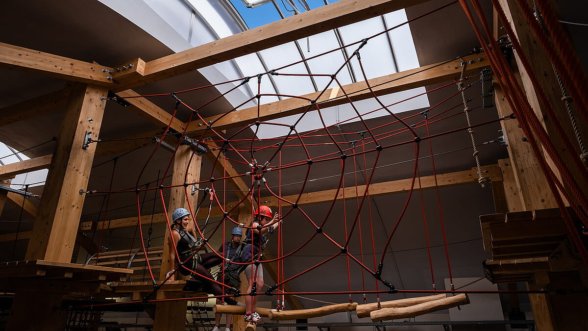 Innenansicht der Kletterhalle "Alte Brauerei" in Eisenach mit LAMILUX Lichtband B und drei Personen auf einem Hochseilgarten mit Kletternetz.
