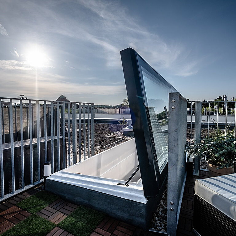 Geöffneter LAMILUX Flachdach Ausstieg Komfort Swing auf begrüntem Dach mit seitlich schwenkender Verglasung und sicherem Dachzugang