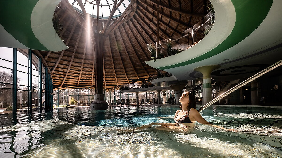 Innenbereich der Soletherme Solemar in Bad Dürrheim mit großer Glaskuppel und einer Frau, die entspannt im Wasser schwimmt.