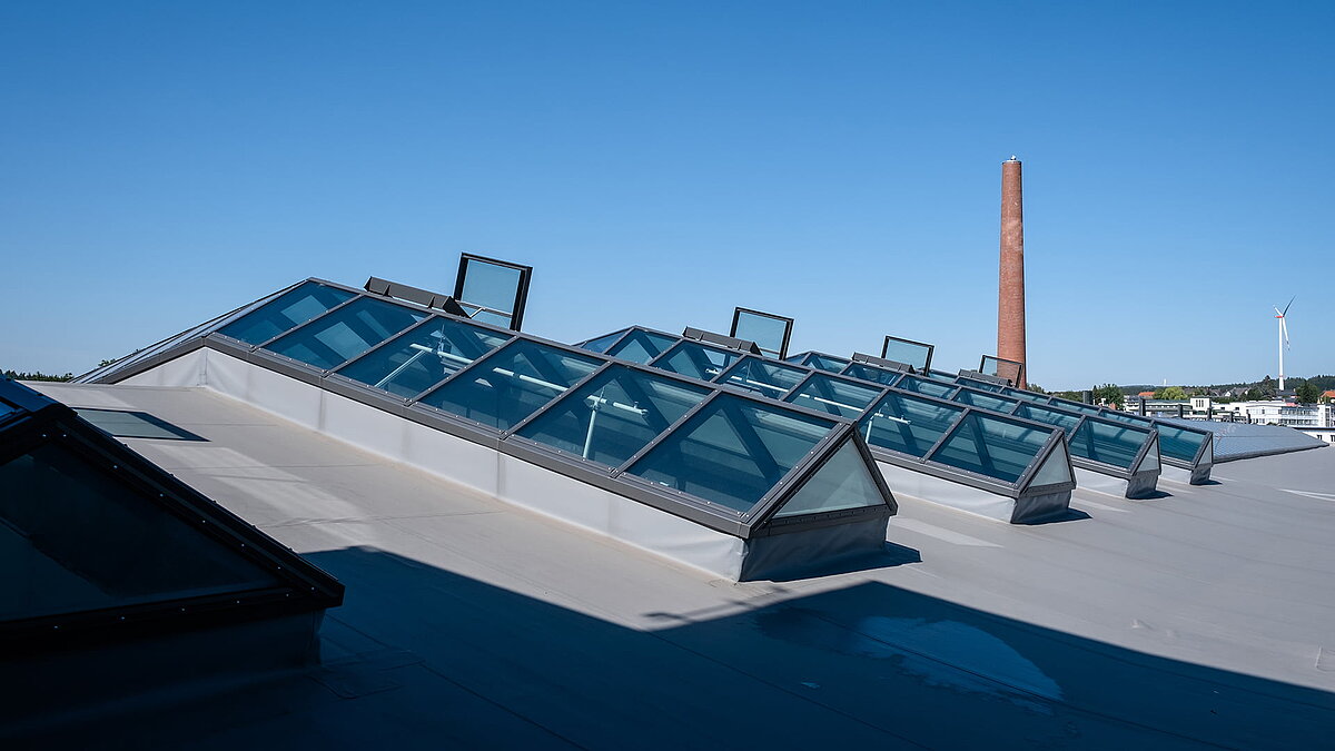 Glasdach PR60 des Outlet Centers Selb mit geöffneten Fensterelementen und Schornstein im Hintergrund.
