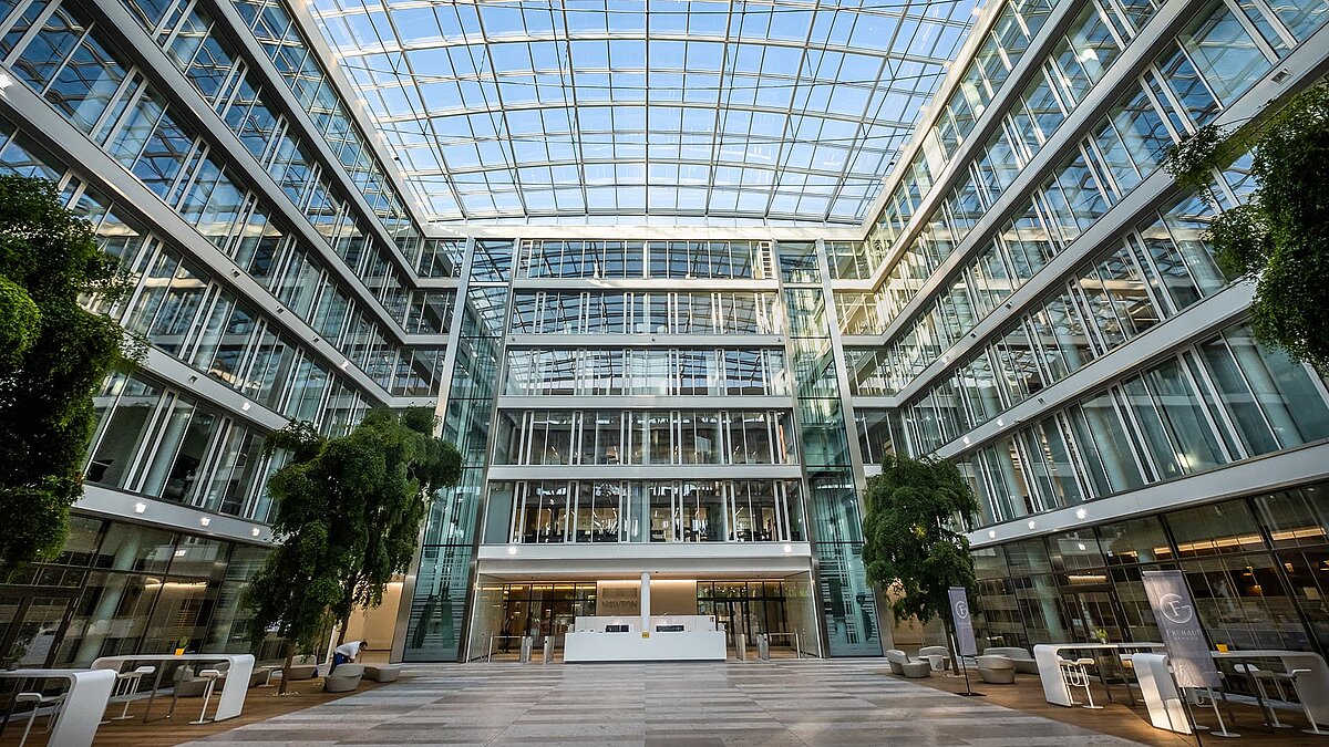 Innenansicht des Bürogebäudes Newton der TÜV Süd Gruppe mit modernem Glasdach, großen Fenstern und begrüntem Atrium.