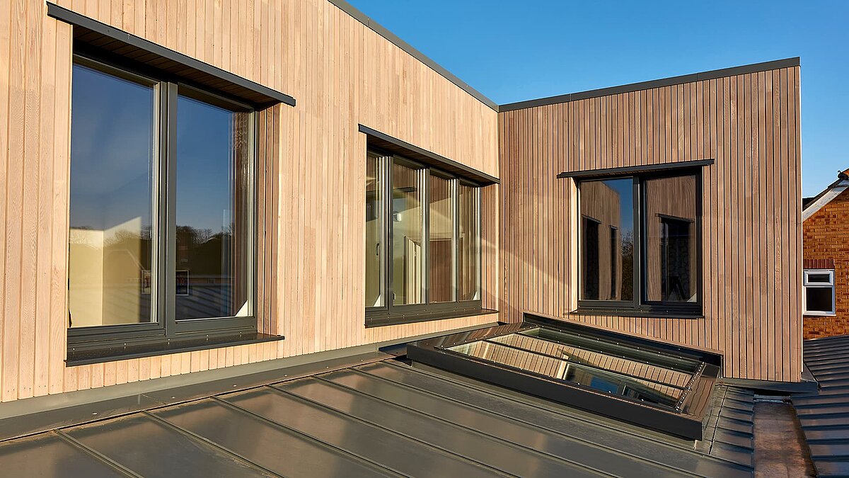 Außenansicht des modernen Gebäudes der Potton Show Homes in England mit LAMILUX Glasdach PR60, Holzfassade und großen Fenstern im warmen Abendlicht.