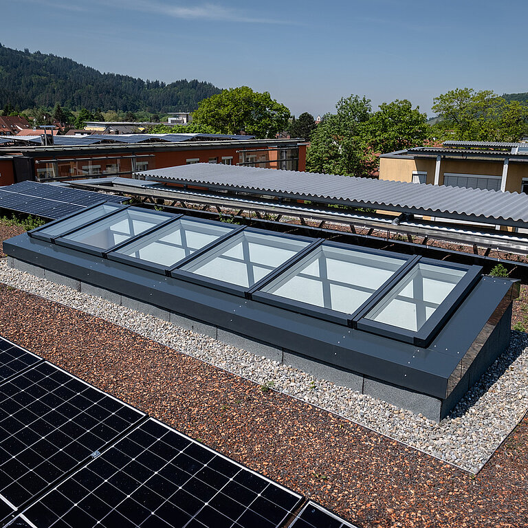 Modulares Glasdach MS78 auf begrüntem Flachdach mit umliegenden Solarpanels.