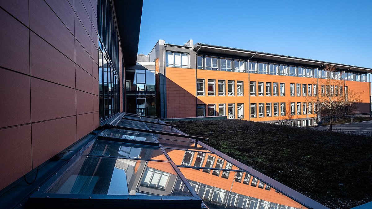 Schulzentrum Rehau mit reflektierendem LAMILUX Glasdach PR60 und begrüntem Dachbereich im Vordergrund.