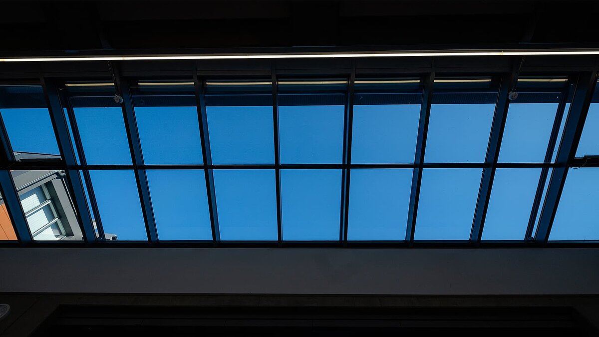 Blick von unten auf das LAMILUX Glasdach PR60 im Schulzentrum Rehau, durch das der blaue Himmel sichtbar ist.