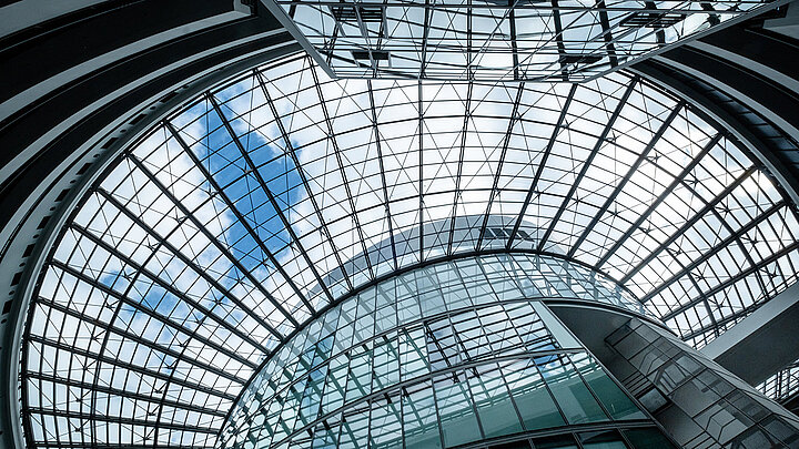 Modernes geschwungenes Glasdach mit Stahlkonstruktion und blauem Himmel in modernem Gebäude