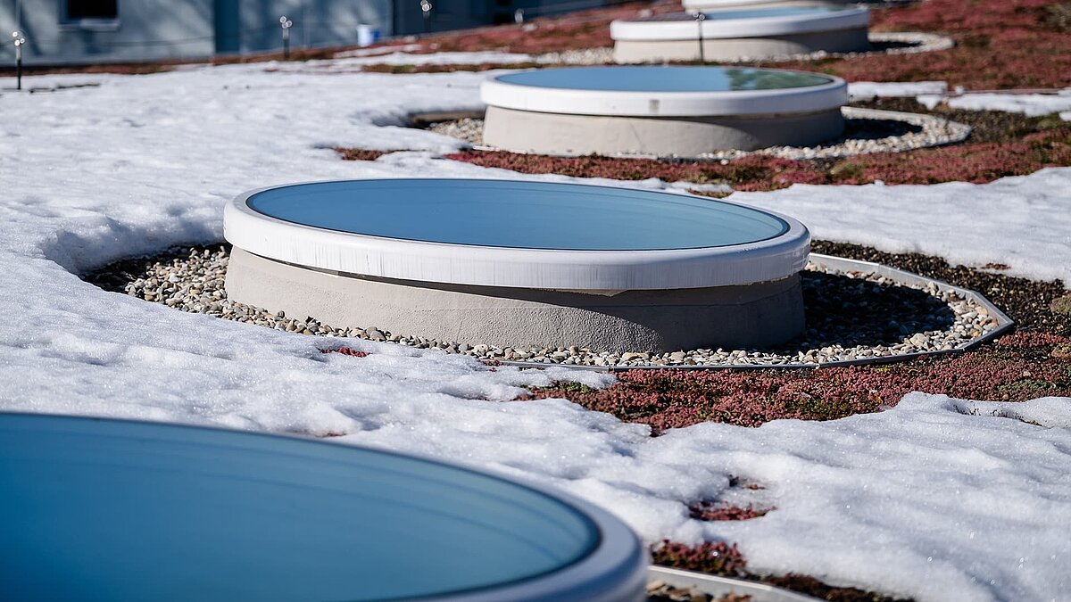 Runde Flachdach-Fenster auf dem begrünten und schneebedeckten Dach des Kindergartens St. Severin.
