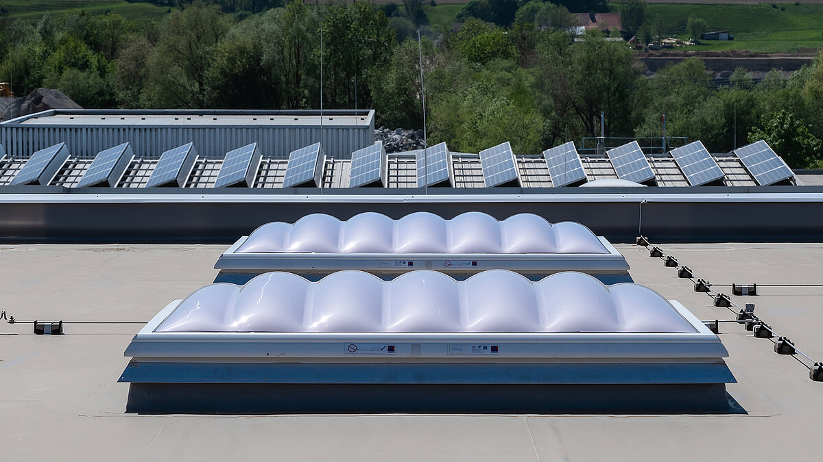 LAMILUX Lichtkuppeln F100 W auf dem Dach der Produktionshalle des Bauunternehmens Unglehrt, im Hintergrund LAMILUX Lichtbänder B und Solarpaneele.