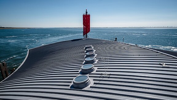 Dach des Hafenterminals Norderney mit runden Oberlichtern, die Tageslicht einlassen, vor der Kulisse des Meeres.