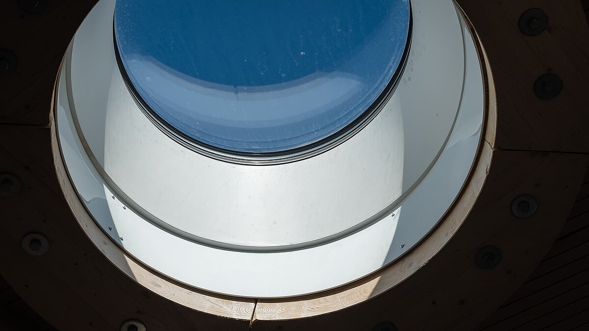 Nahaufnahme eines runden Oberlichts im Hafenterminal Norderney mit Holzrahmen und Glasoberfläche, durch das Tageslicht einfällt.