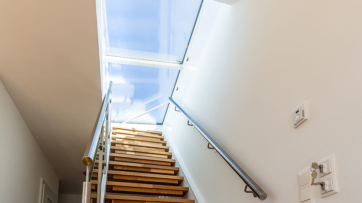 Treppenaufgang in einem Wohnhaus in Korneuburg mit Flachdach Ausstieg und großem Glasdach für natürliche Beleuchtung.