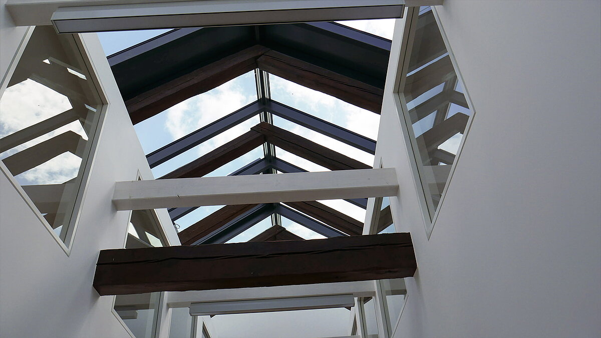 Glasdachkonstruktion mit Holzträgern und weißen Stahlverstrebungen an der Leibniz-Universität Hannover, Blick auf den Himmel.