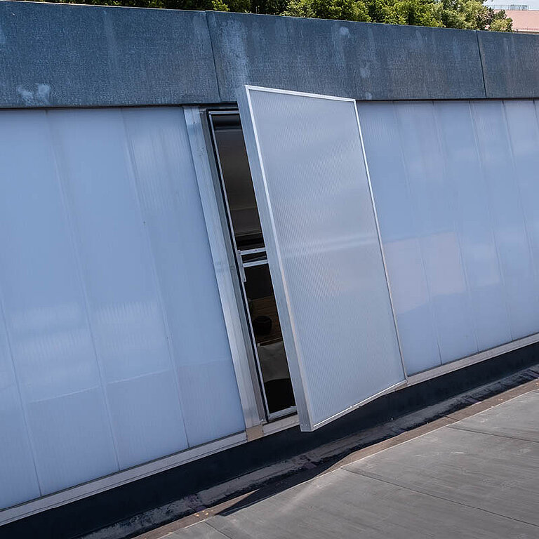 Geöffnetes LAMILUX Lichtband W|R RWA an Dachkante mit seitlich aufgeklapptem Flügel und transluzenter Verglasung