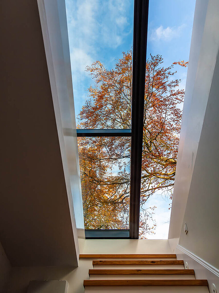 Innenansicht eines LAMILUX Flachdach Ausstieg Komfort Solo mit geöffneter Verglasung, Treppenaufgang und Blick ins Freie mit herbstlichem Baum