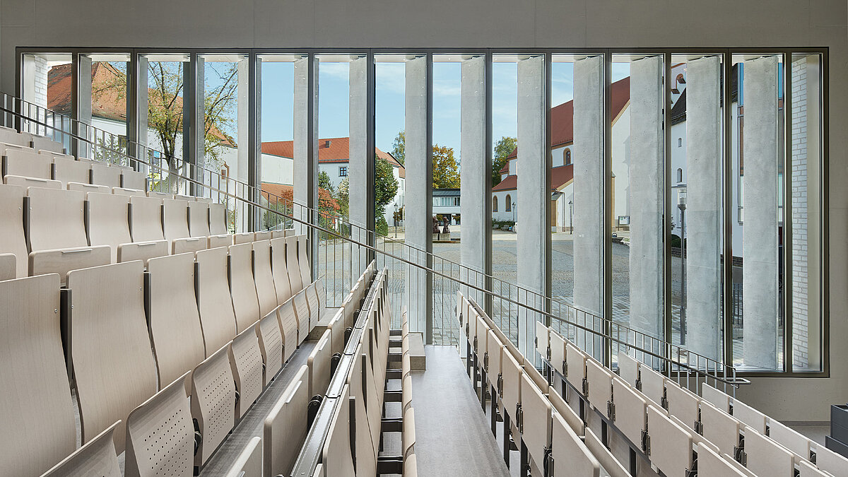 Blick aus einem leeren Hörsaal mit hochgeklappten Stühlen durch ein Glasfenster nach draußen