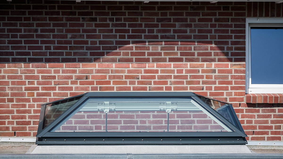 Flachdachfenster FW von LAMILUX an einem Wohnhaus in Hamburg, installiert auf einem Ziegeldach vor einer roten Backsteinfassade.