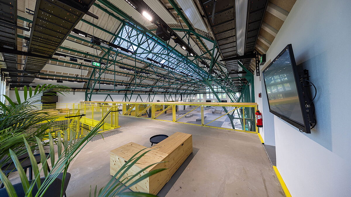 Interior view of an industrial hall with steel structure, glass roof, and modern mezzanine level.