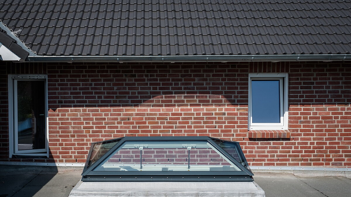 Außenansicht eines Wohnhauses in Hamburg mit einem LAMILUX Flachdach Fenster FW, integriert in eine rote Ziegelwand unter einem Ziegeldach.