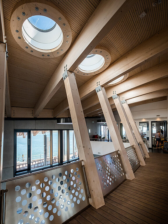 Deckenansicht des Hafenterminals Norderney mit runden Flachdach Fenstern und massiven Holzbalken.