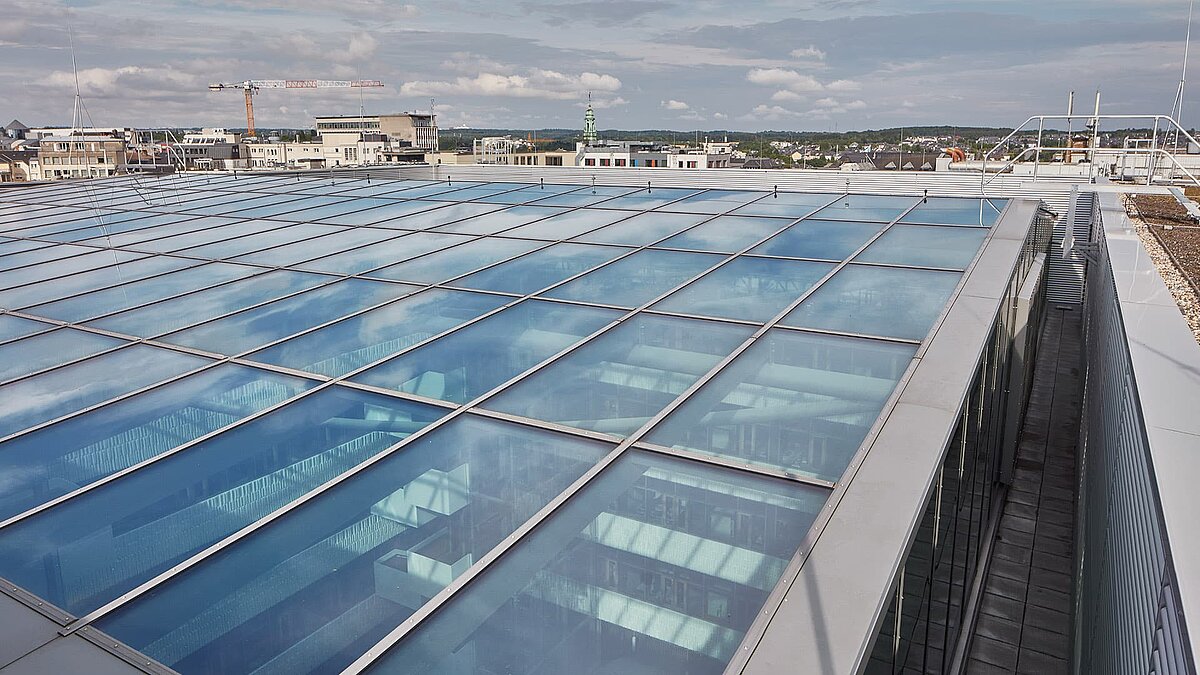 Glasdachkonstruktion des Postgebäudes in Luxemburg mit LAMILUX Glasdach PR60 Passivhaus-System, aufgenommen von außen mit Reflexionen des Himmels.