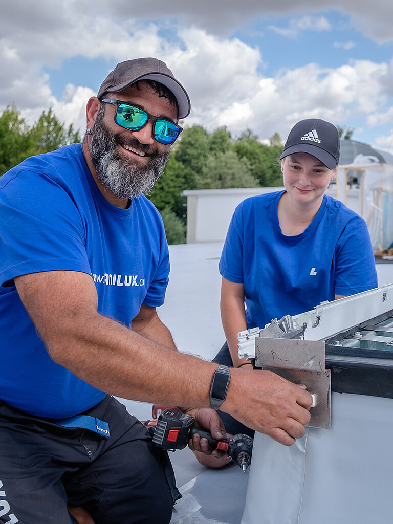 Zwei Handwerker montieren ein Tageslichtelement auf einem Flachdach