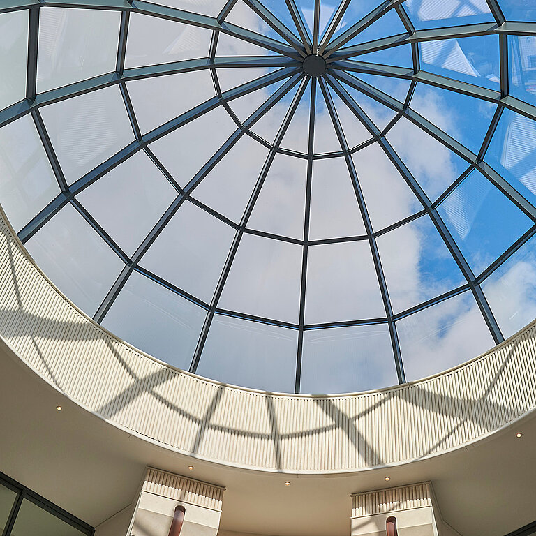 Rundes Glasdach mit filigraner Stahlkonstruktion, das von unten betrachtet großzügig Tageslicht in den Innenraum lenkt.