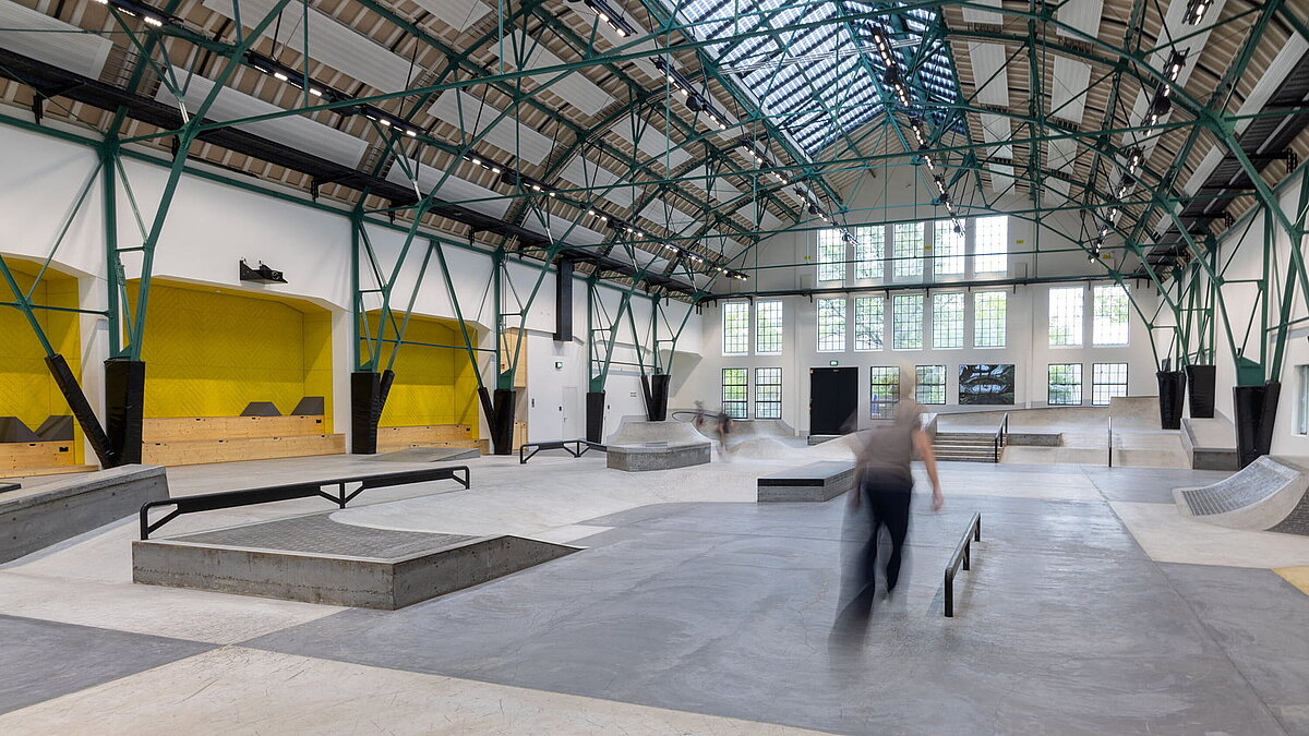 Skatehalle in renovierter Industriehalle mit Glasdach PR60 und grüner Stahlkonstruktion.
