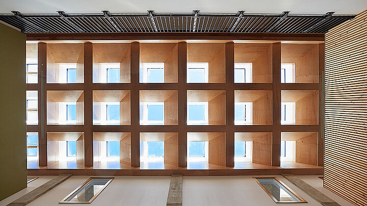 Innenansicht eines Atriums mit Holzlamellen und quadratischen Fensteröffnungen